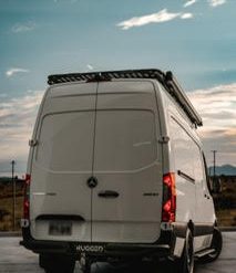 White Mercedes-Benz 144 Wheelbase High Roof Sprinter van with aftermarket rear bumper by Rugged Design Concepts, matte black aluminum, rear step integrated, overlanding accessory